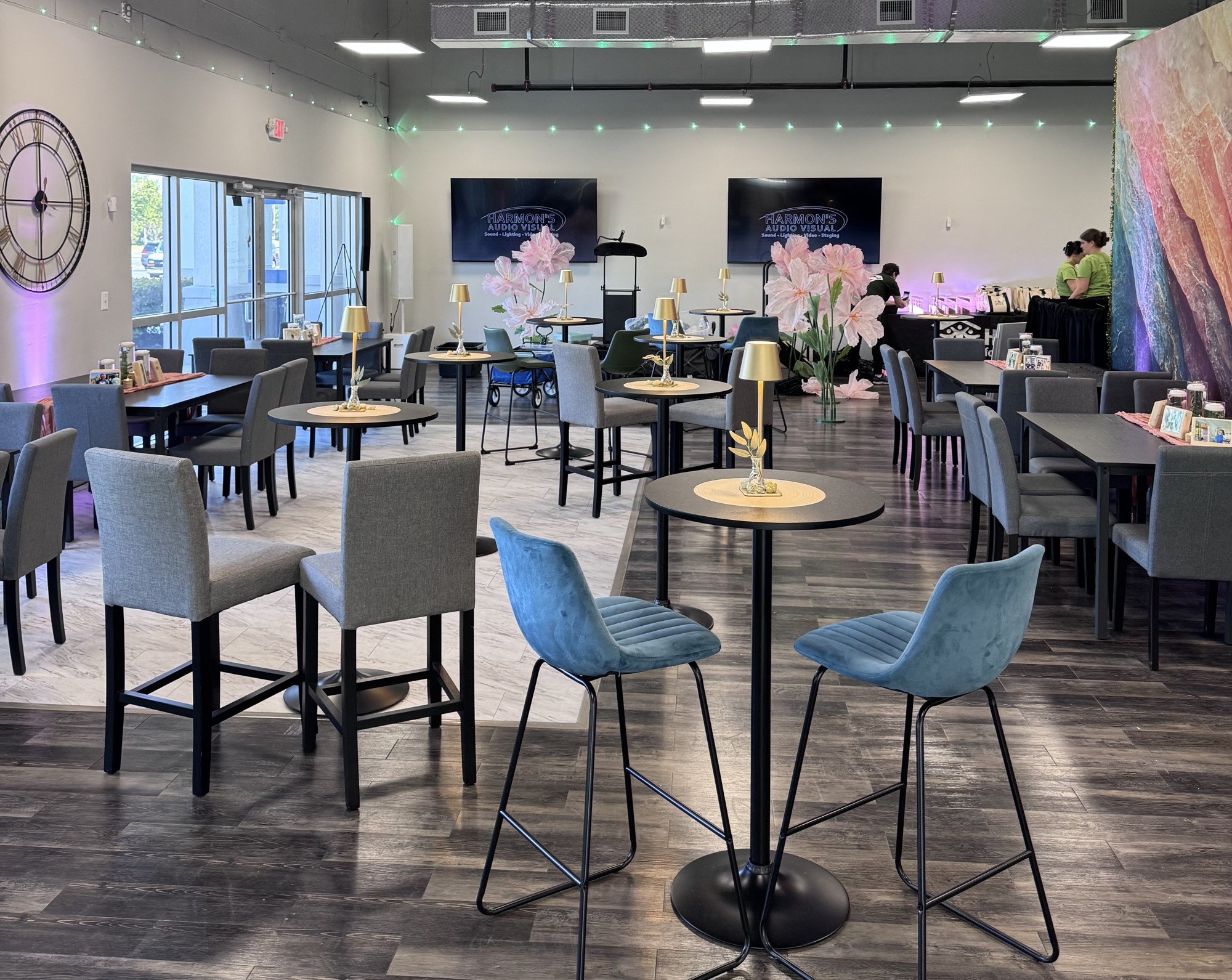 B Hive arranged with cocktail tables, blue and gray seating, gold lamps and pink floral accents, with the colorful feature wall on the right.